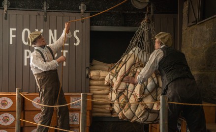 Two men in vintage attire lift sacks in a net at the exhibition.