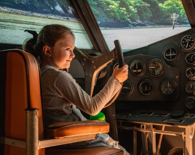 Smiling girl sits in cockpit of Airplane, holding the control column.